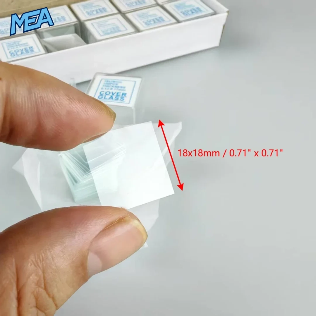 Hand holding an 18x18mm microscope cover glass slide with dimension markers showing true-to-size measurement